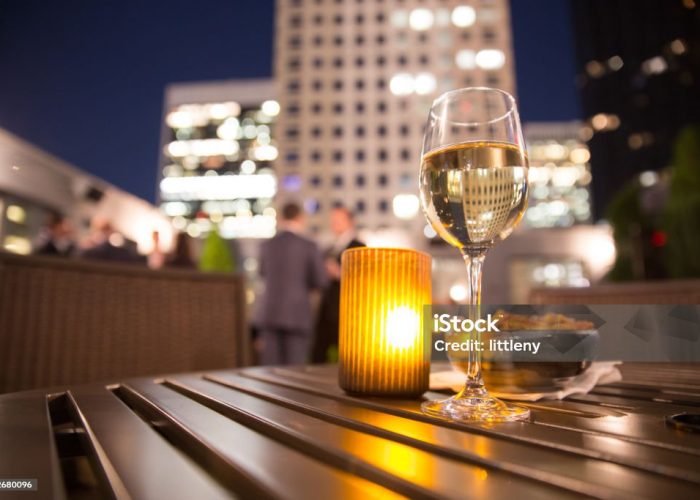 Glass of white wine and candle with evening view of city buildings